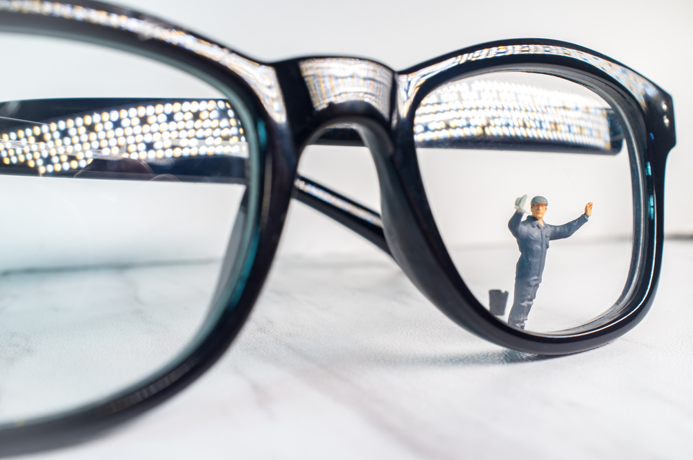 A zoomed in eyeglasses with a miniature man wiping the lense