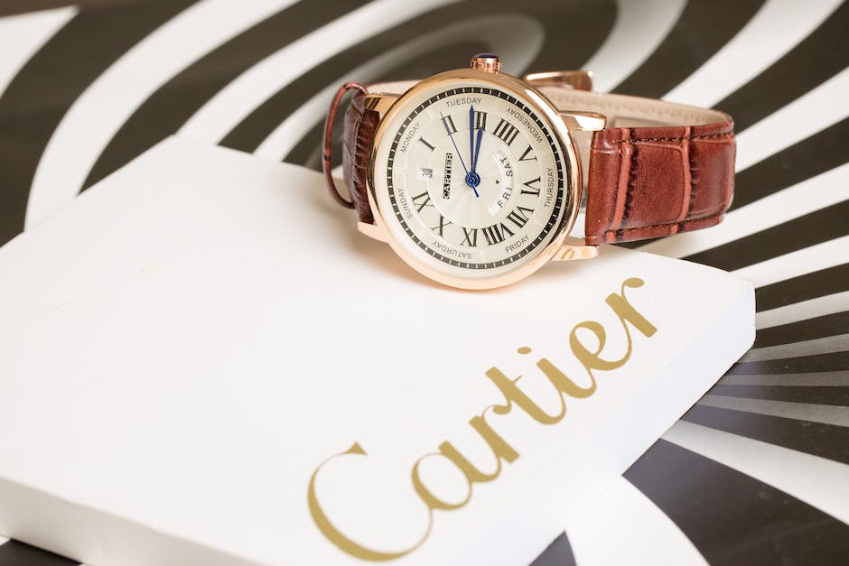 A cartier watch with brown leather strap put on top of a paper with Cartier logo on it