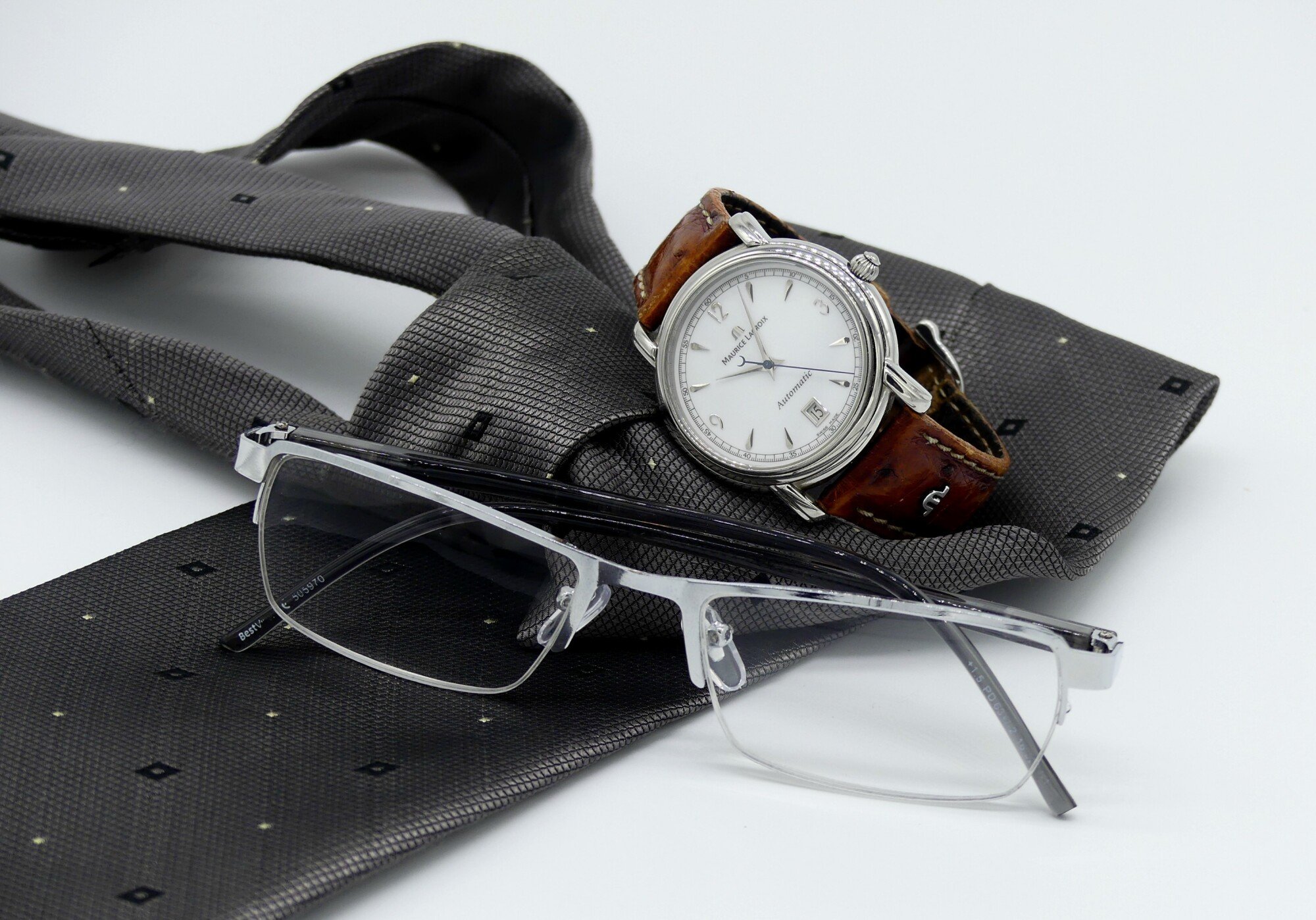 Eyeglasses beside a wrist watch together with black suit tie