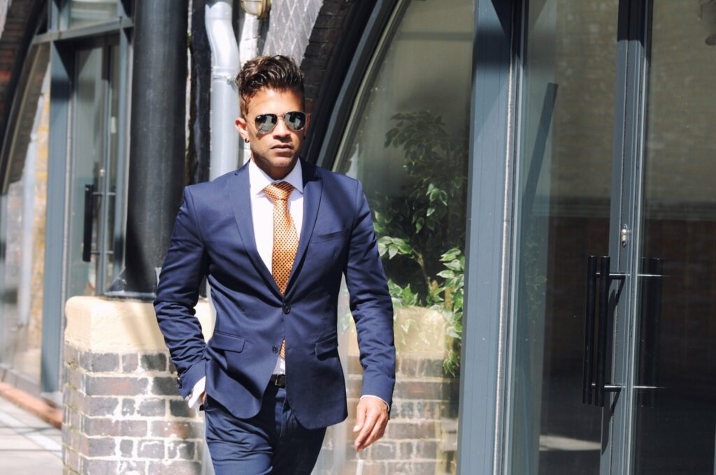 A man walking while wearing a business suit and designer sunglasses
