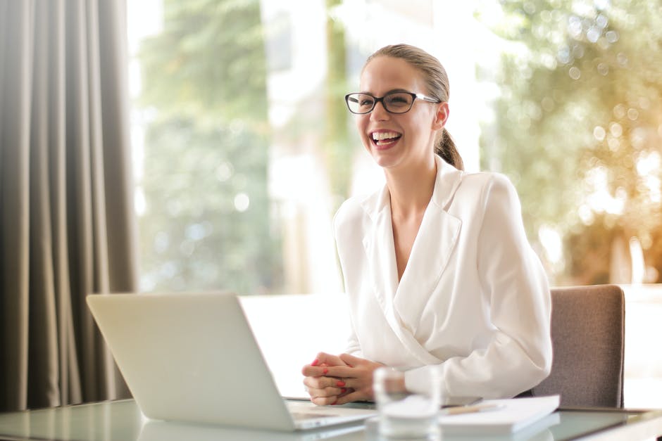 A woman laughing wearing eyeglasses in front of her laptop