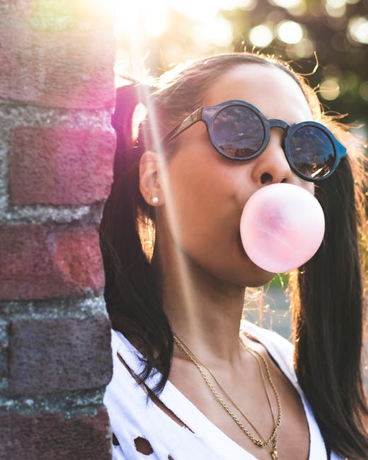 a woman wearing sunglasses blowing a bubble gum