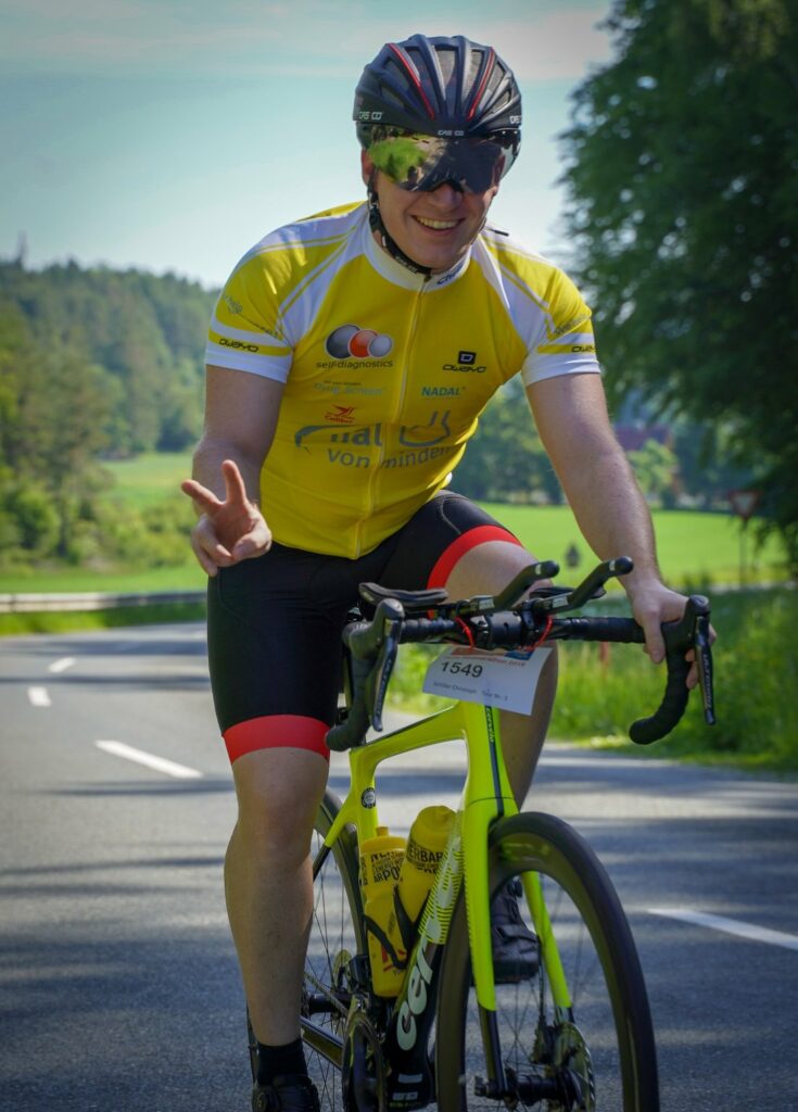 A smiling cyclists wearing yellow cycle suit and sports glasses